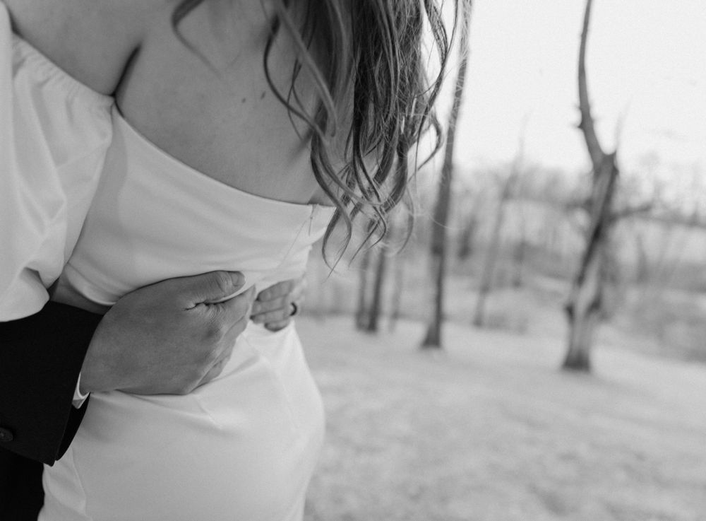 A close-up black and white shot showing someone holding a ring outdoors with bare trees in the background.