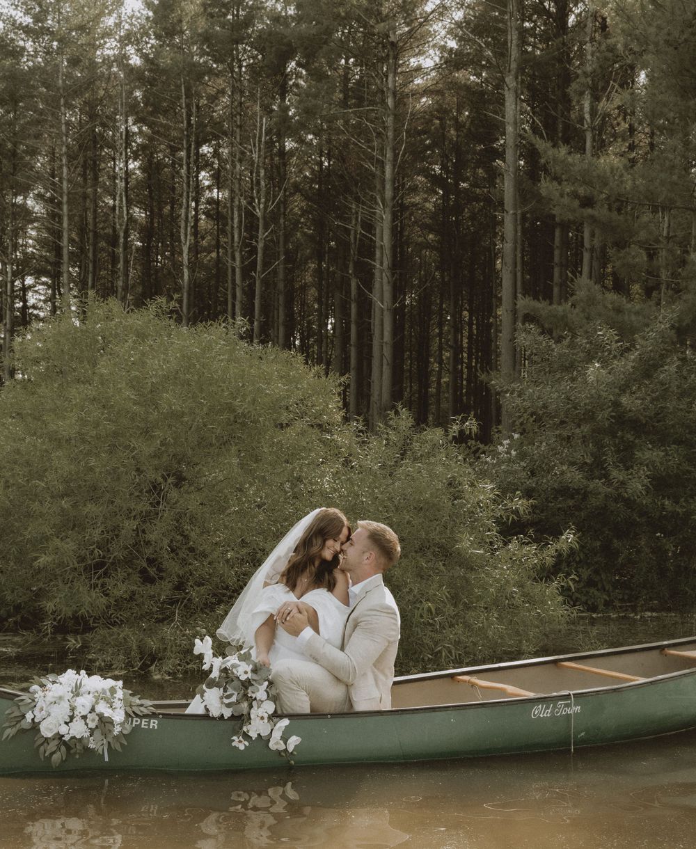 A romantic moment captured of a couple in a canoe surrounded by pine trees.