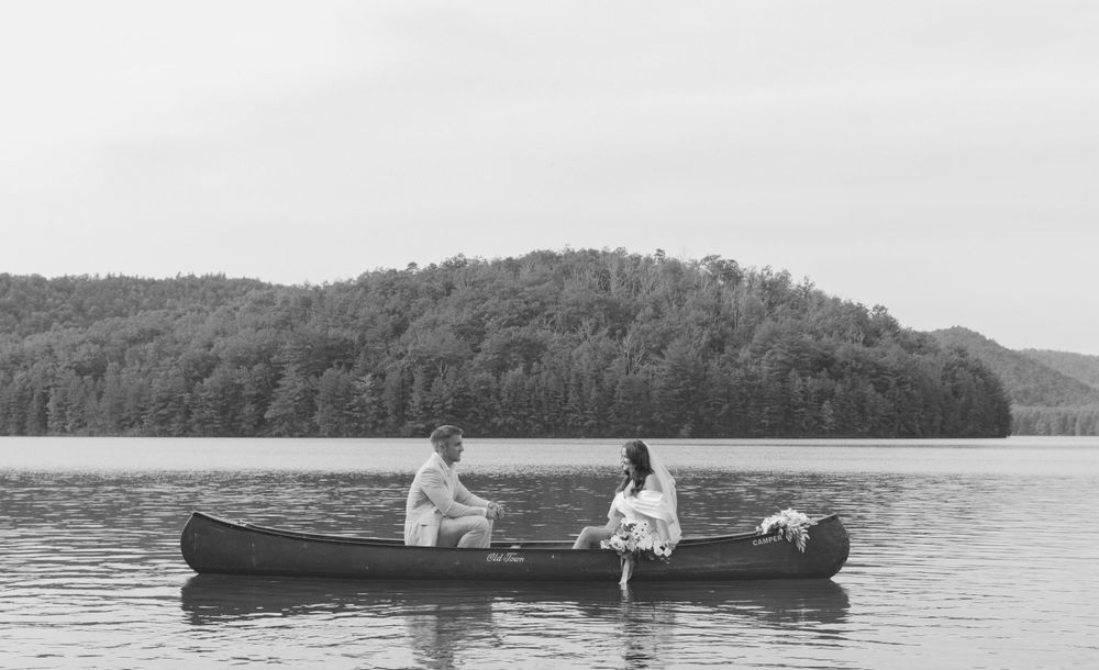 A couple sits in a vintage canoe on a serene mountain lake surrounded by forested hills.