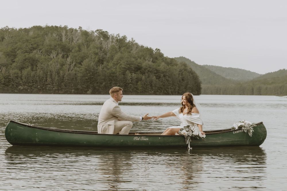 A couple shares an intimate moment while sitting in a green canoe on a tranquil lake.