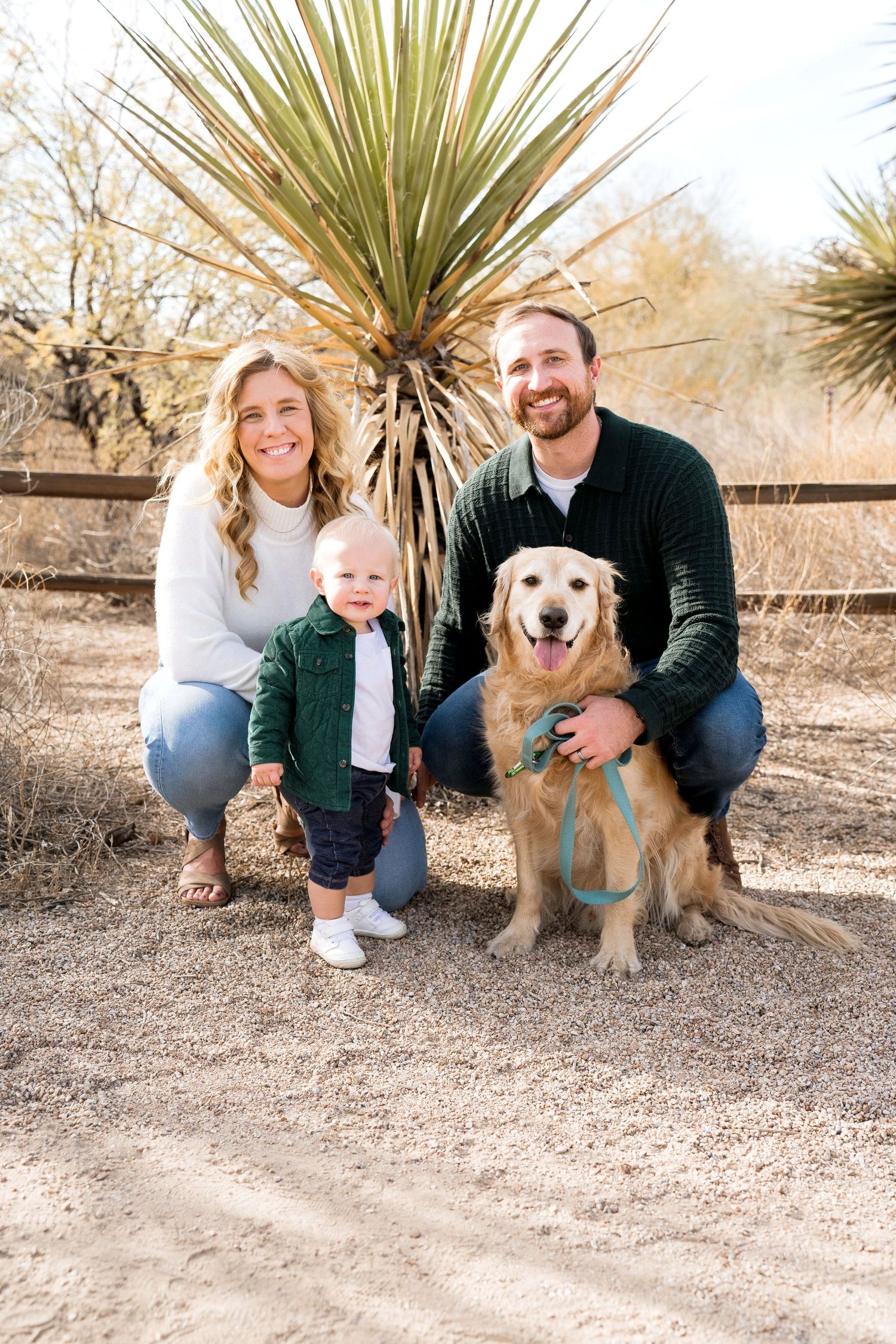 Outdoor family portrait with a golden retriever dog in front of desert plants.