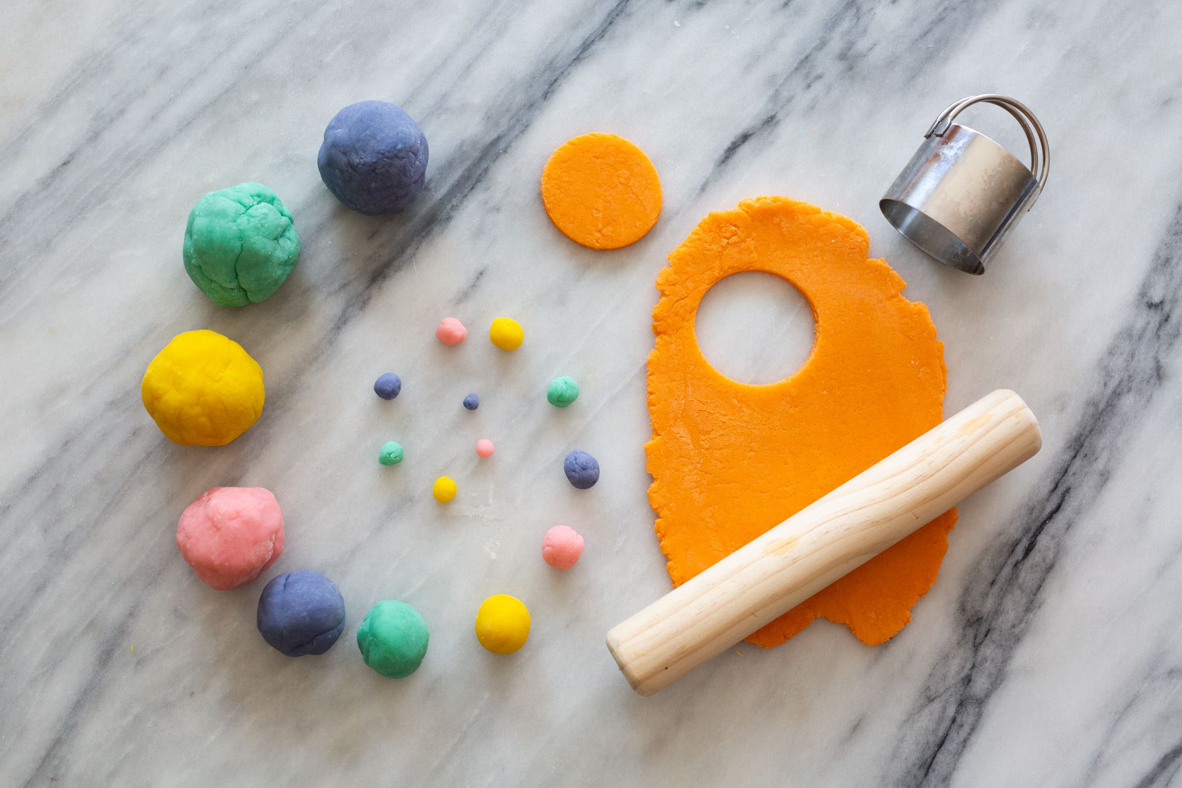 Colorful playdough balls and crafting tools arranged on marble surface.