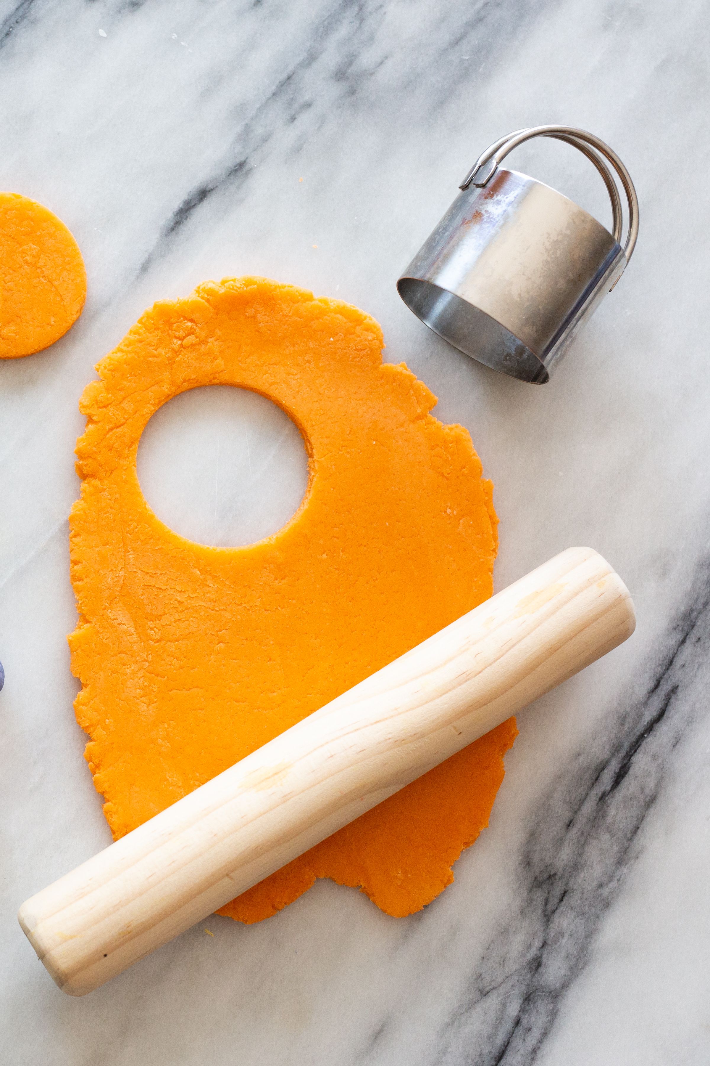 Rolling pin and baking tools with orange dough on marble countertop.