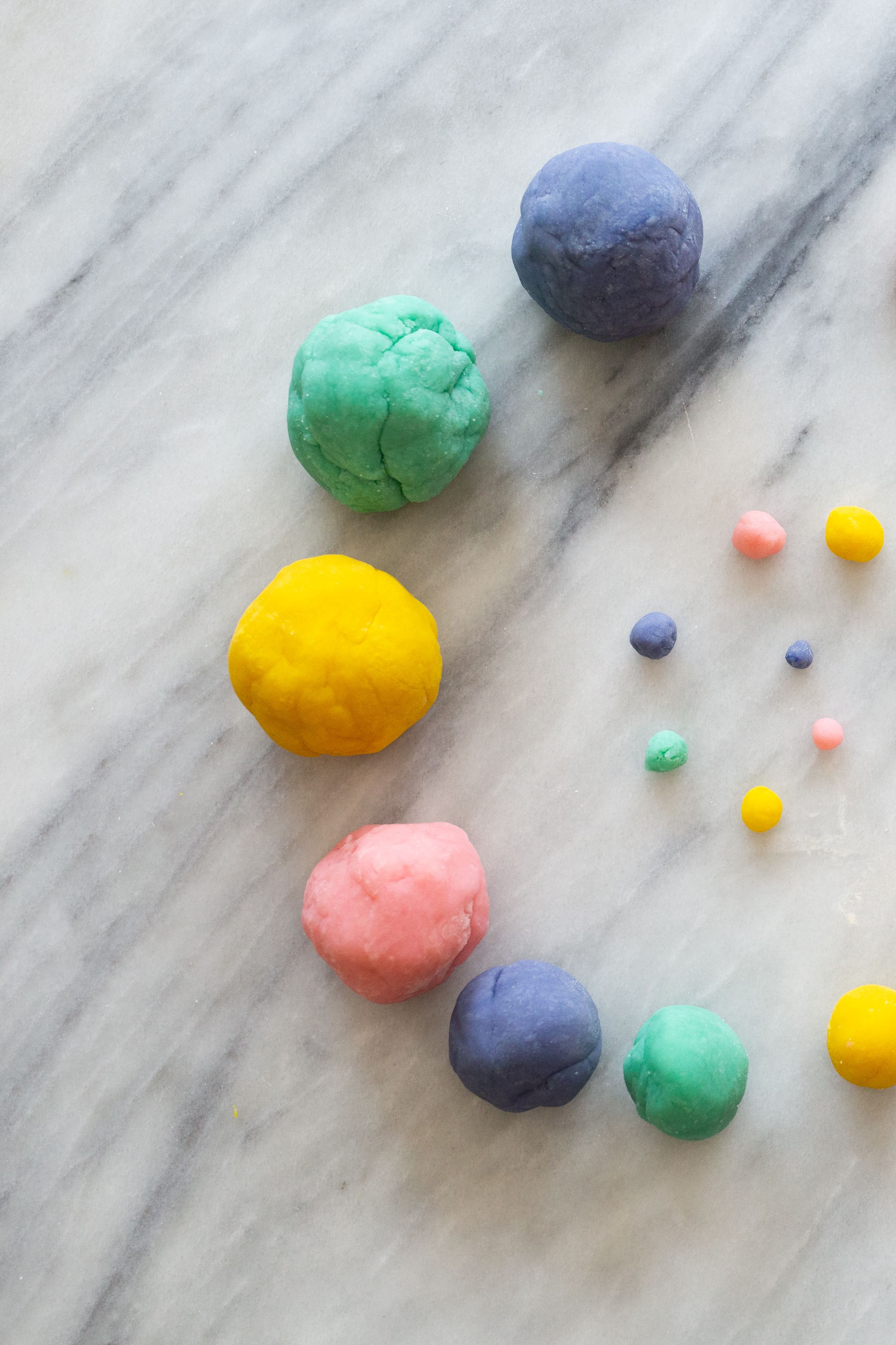 Colorful balls of playdough in blue, green, yellow, and pink arranged on marble background.