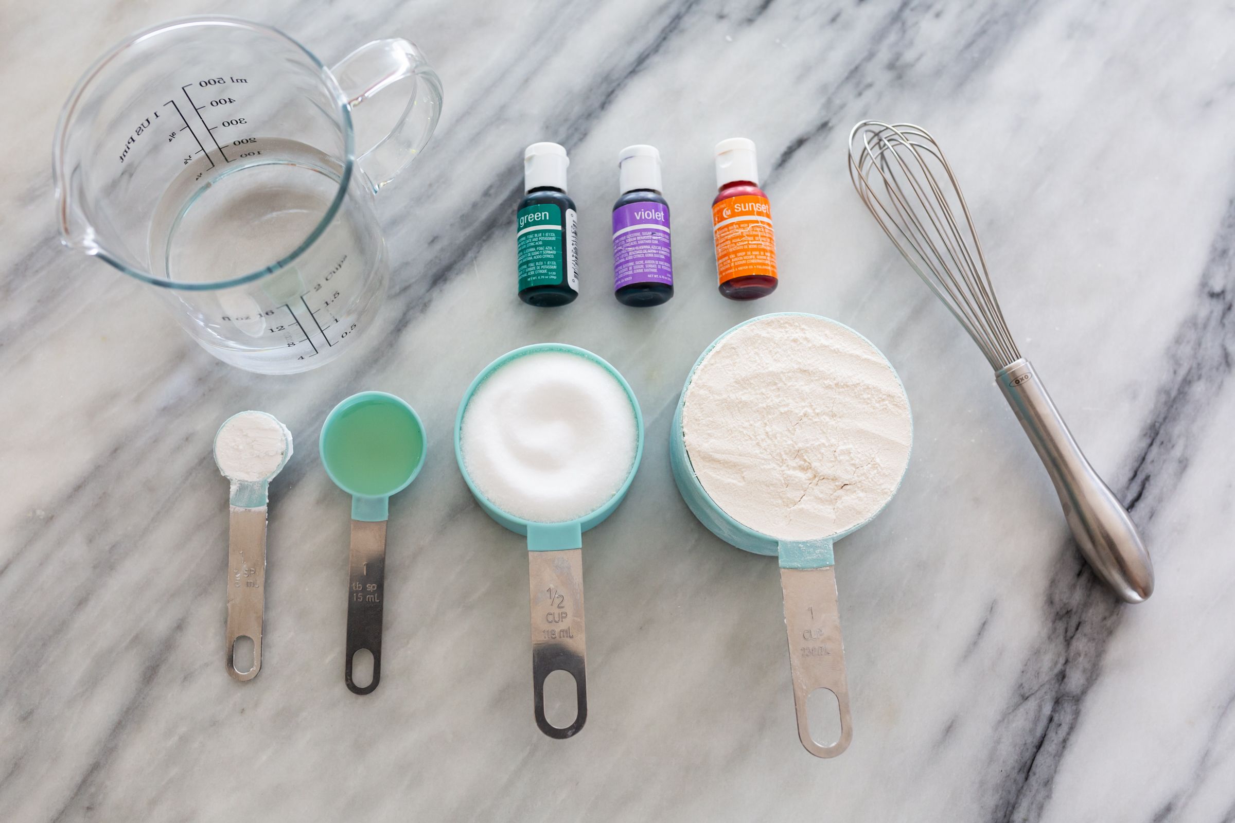 Baking ingredients and measuring spoons with essential oils on marble counter.