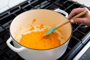 Mixing bright orange batter in white dutch oven on gas stovetop.