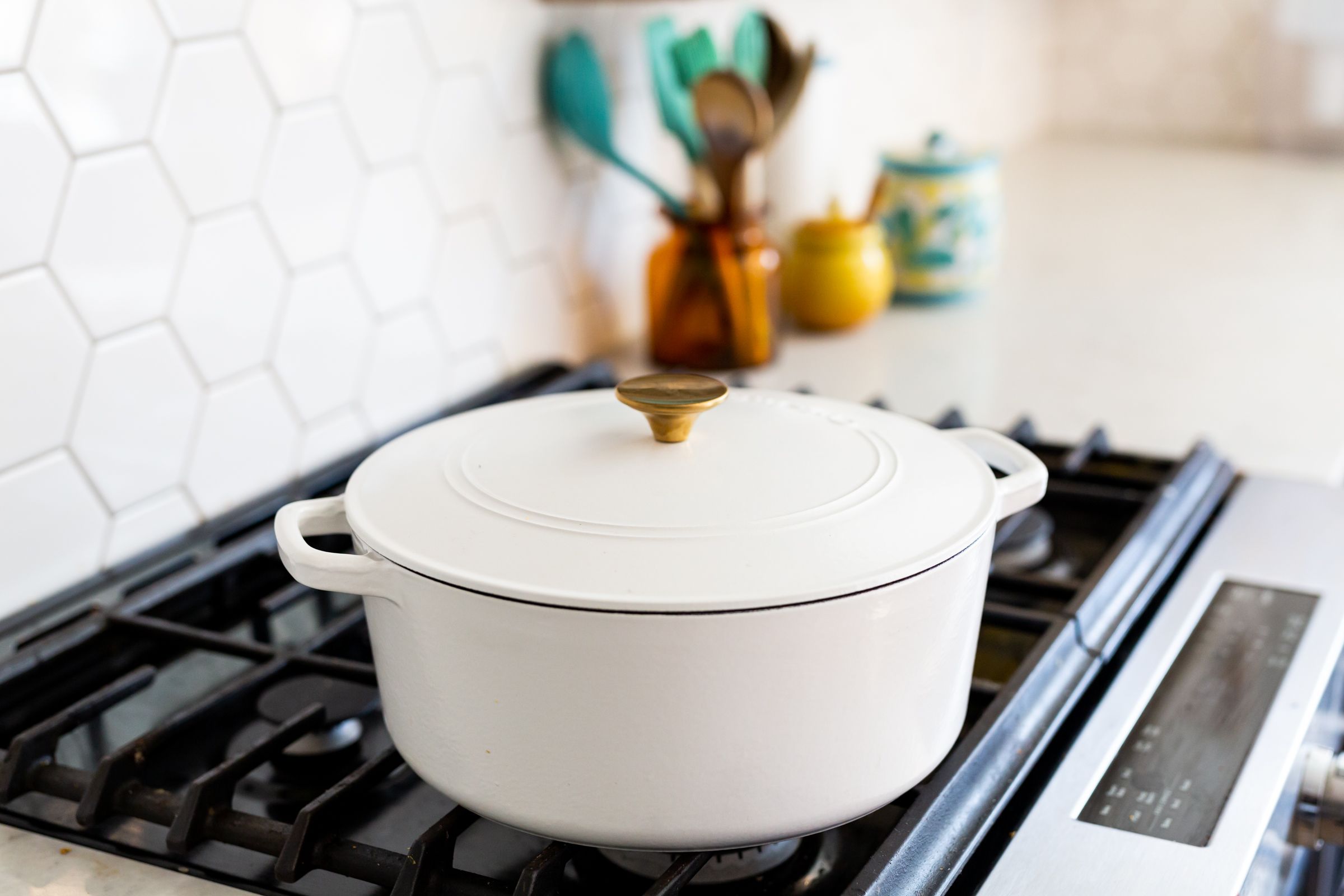 White enamel Dutch oven on gas stovetop with hexagonal tile backsplash.