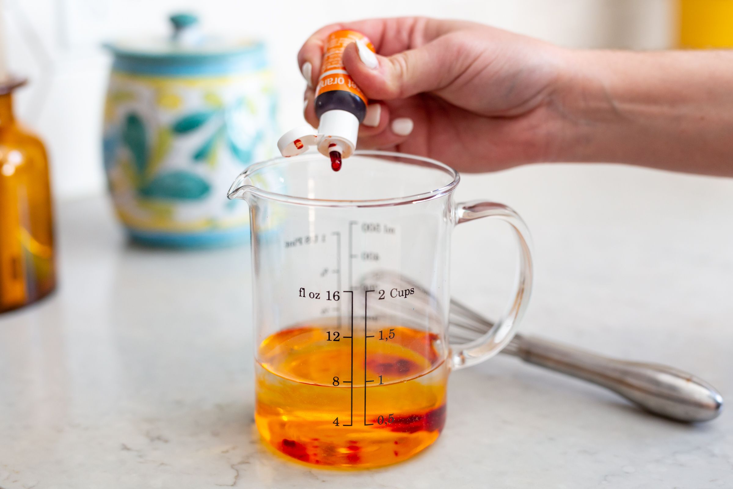 Orange liquid being measured in a glass measuring cup with teapot in background.