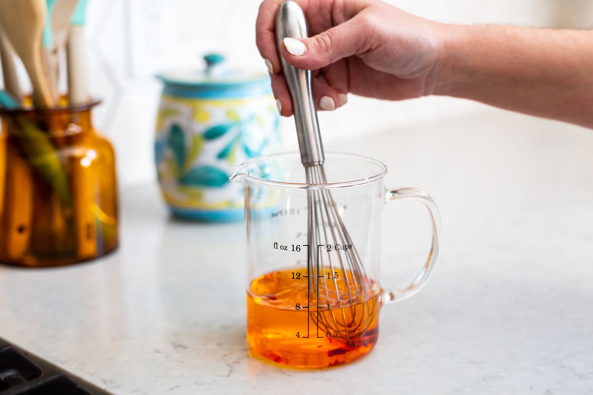 Whisking orange liquid in a glass measuring cup on white countertop.