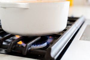 White pot heating on gas stove burner with blue flame.