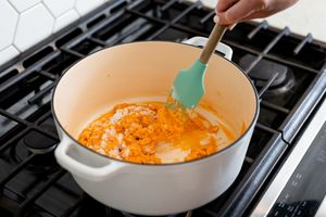 Stirring orange mixture in white pot with turquoise spatula on stovetop.