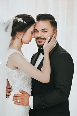 Intimate moment between newlyweds in formal attire against white background.