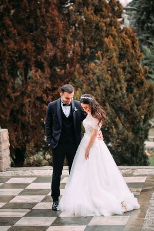 Elegant couple in wedding attire walking on a checkered outdoor terrace.