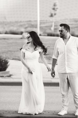 A black and white candid photo of a couple in white outfits walking outdoors.