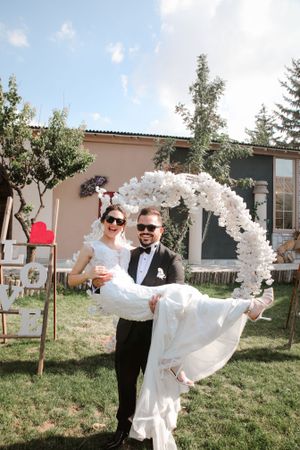 Wedding couple celebrating under a white balloon arch in an outdoor garden setting.