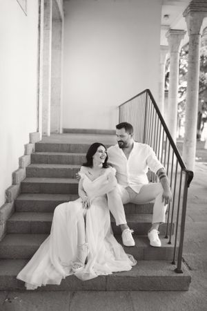 A black and white photo of a couple seated on stone steps with architectural columns.