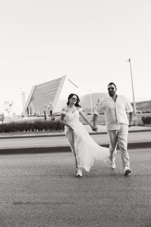 A black and white photo of a couple walking together on a street with modern architecture in the background.