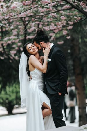 Romantic wedding photo of couple embracing under blooming cherry blossom trees.