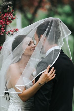 Romantic kiss under wedding veil with red flowers blooming in background.