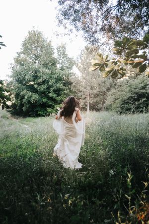A bride in a flowing white dress running through a sunlit meadow.