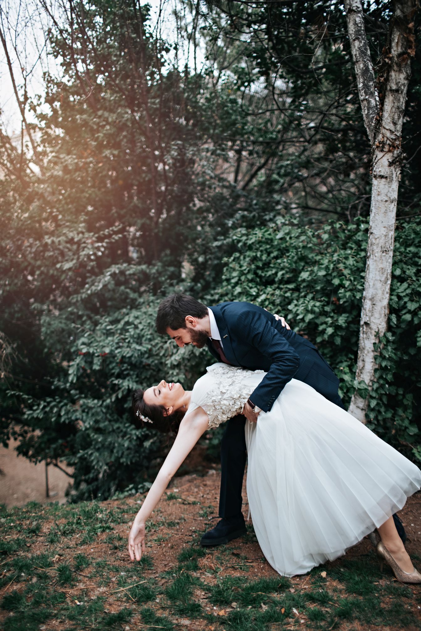 A romantic dip pose between a couple in wedding attire surrounded by trees.