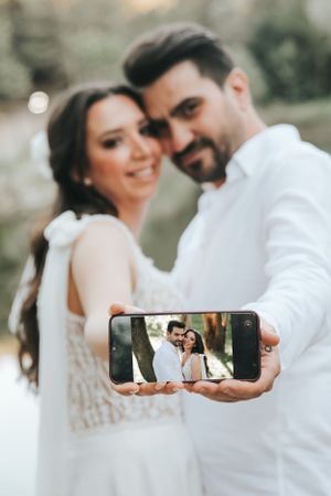 A couple taking a selfie during their wedding photoshoot outdoors.
