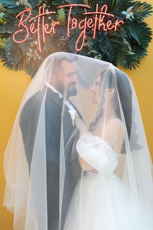 A romantic wedding portrait under a neon 'Better Together' sign with tropical foliage.