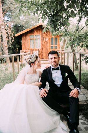 Newlyweds relaxing on wooden deck with rustic cabin in background.