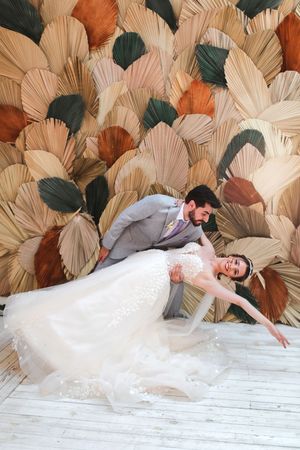 A creative wedding photo against a decorative fan-patterned backdrop in earthy tones.