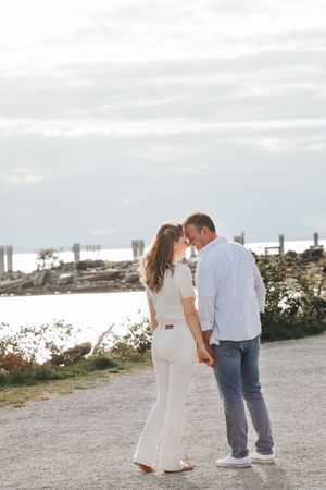 A couple shares an intimate moment on a coastal path at sunset wearing coordinating white outfits.