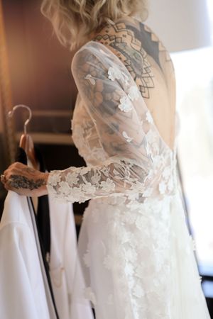 Close-up detail of delicate lace sleeve on a white wedding dress with intricate floral embroidery patterns.