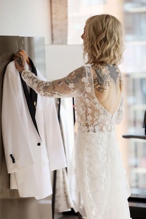 A white wedding dress and suit jacket hang side by side, showcasing delicate lace details and elegant tailoring.