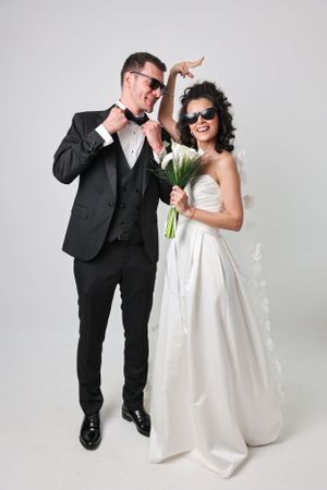 A fun wedding photo with a couple in matching sunglasses posing playfully against a white background.