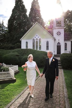 A couple walks hand in hand on a brick path in front of a charming white chapel.