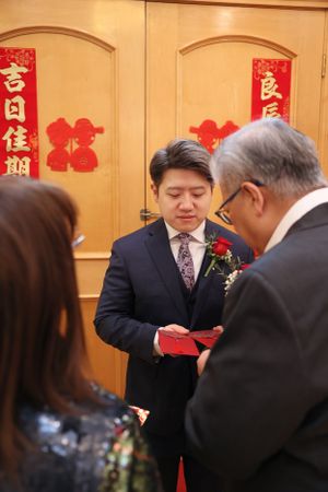 Traditional Chinese wedding ceremony with red decorations and people exchanging red envelopes in formal attire.