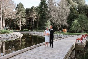 A couple stands together on a wooden bridge over a peaceful pond.