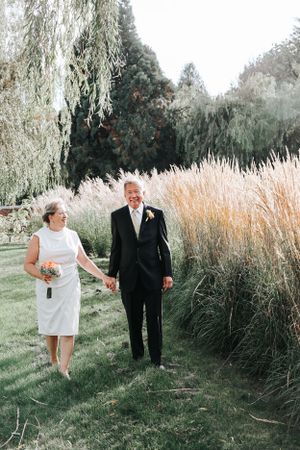 A couple walks hand in hand through a garden with ornamental grasses.