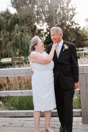 A happy couple shares a tender moment by a wooden railing outdoors.