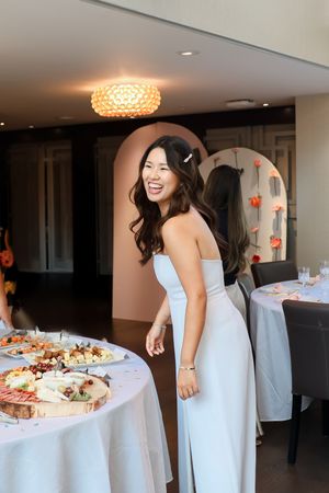 People in white dresses gather around a table with appetizers and snacks at an indoor event.