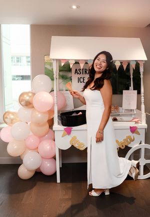 White decorative cart with balloon arch in pink, white and gold colors set up for a party with Astro Ice signage.