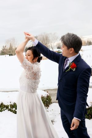 A couple dancing in the snow on their wedding day, with the bride wearing a lace gown and groom in navy suit.