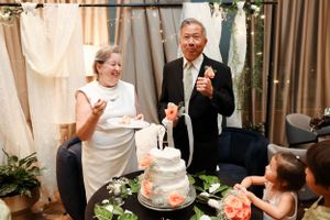 Wedding cake cutting celebration with decorative floral arrangements at an elegant indoor venue.