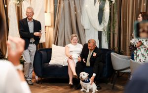 Casual celebratory moment in an event space with displayed wedding dresses and a small dog.
