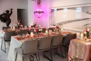 Elegant dining room setup with pink lighting, white chairs, and floral table decorations for a special event.