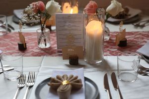 Elegant table setting with glowing candles, roses in vases, and place settings on white tablecloth with menu card.