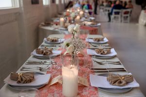 Long elegant dining tables set with white plates and pink floral centerpieces in a bright event space.