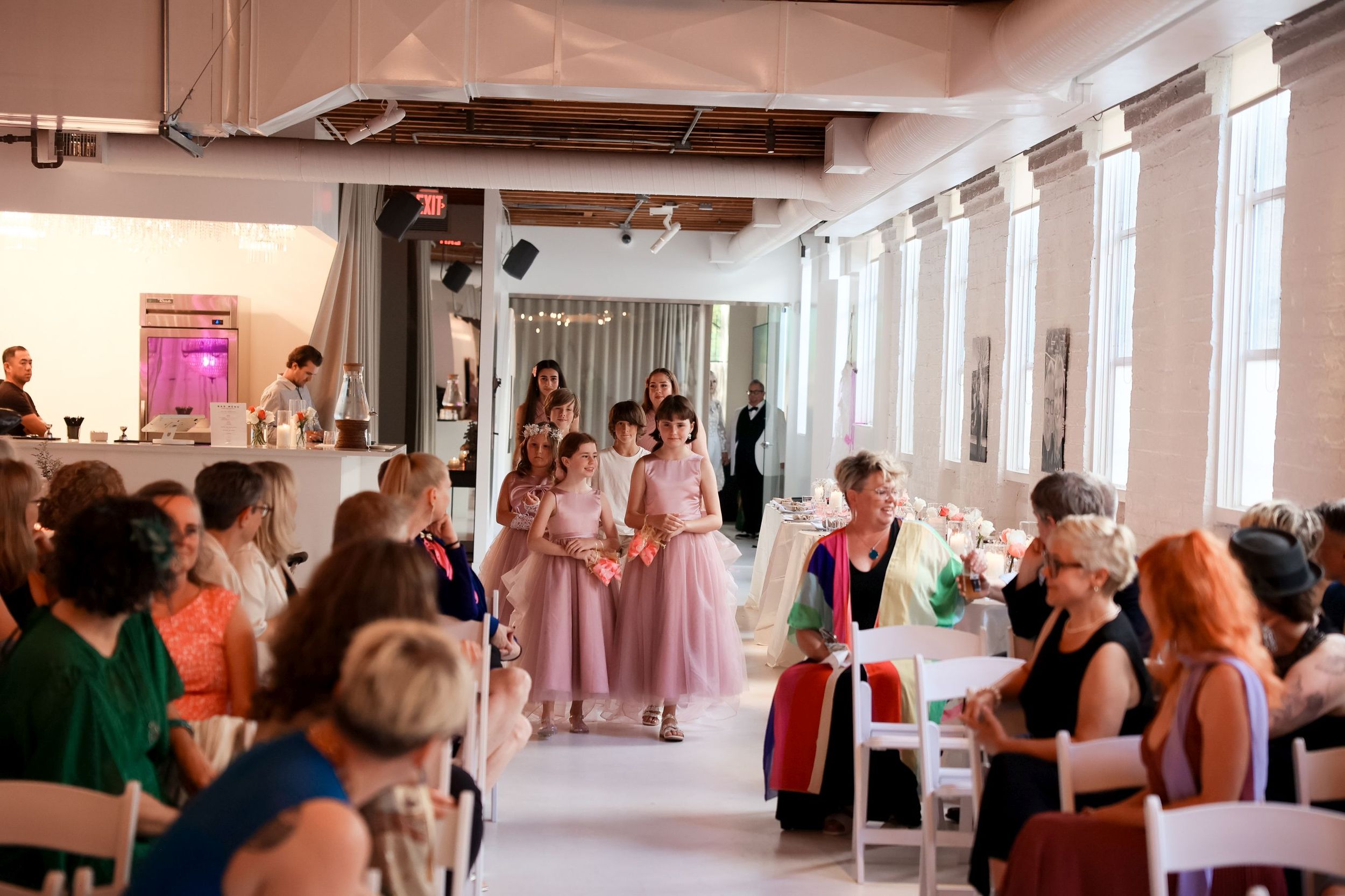 People gathered in a bright indoor space with white walls and exposed wooden beams during a social event.