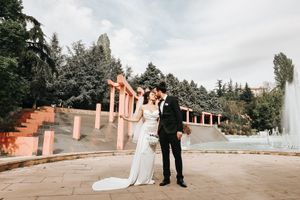 Newlyweds celebrate their wedding day in front of pink pillars and fountain.