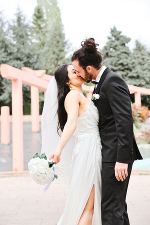 Romantic wedding kiss captured in front of coral-colored columns with evergreen backdrop.