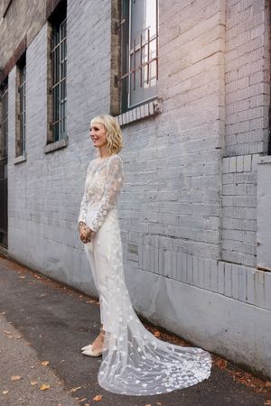 Series of photos showing a bride in a white lace wedding dress with a long train against a white brick wall.